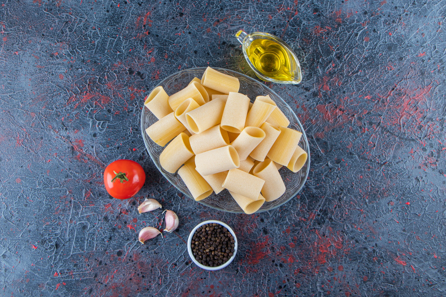 A glass plate of raw cannelloni pasta with garlic and oil on a dark surface